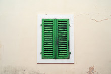 Old Closed Green Wooden Shutters On Light Plastered Wall With Cracks And Time Spots, In Mediterranean Style. Outdoors, Cozy Vintage, Copy Space