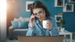 © MYDAYcontent - Focused young woman holding cup and touching glasses looking at laptop screen, livingroom background