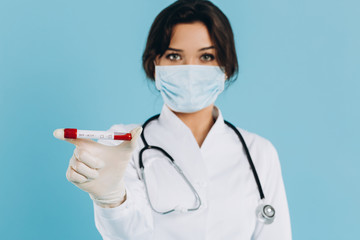 A female doctor in a mask holds test tubes, blood tests, potentially infected people with a coronavirus. Сovid-19 concept