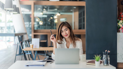 Wall Mural - Happy young asian businesswoman sitting on her workplace in the office. Young woman working at laptop in the office.