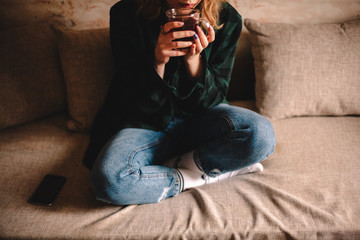 Wall Mural - Young woman drinking tea while sitting on sofa at home