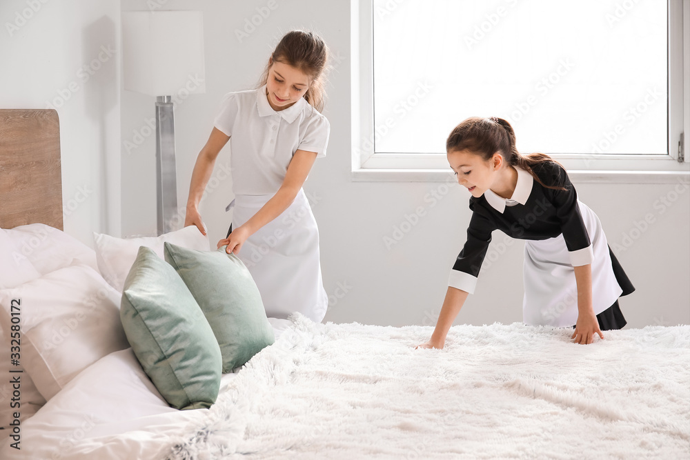 Cute little chambermaids making bed in hotel