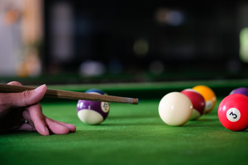 Man's hand and Cue arm playing snooker game or preparing aiming to shoot pool balls on a green billiard table. Colorful snooker balls on green frieze.