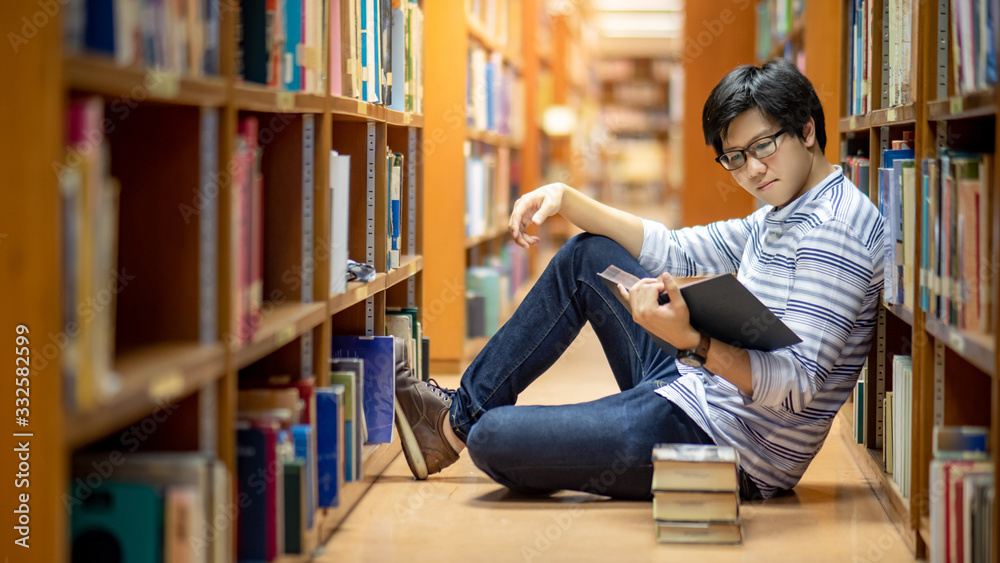 Smart Asian man university student wearing glasses reading book by vintage bookshelf. Textbook resources in college library for educational subject and research. Scholarship for education opportunity. - obrazy, fototapety, plakaty 