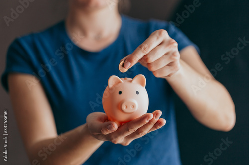 Fotografía female hands hold a pink piggy bank and puts a coin there