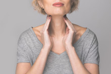 Female Checking Thyroid Gland By Herself. Close Up Of Woman In White T- Shirt Touching Neck With Red Spot. Thyroid Disorder Includes Goiter, Hyperthyroid, Hypothyroid, Tumor Or Cancer Health Care.