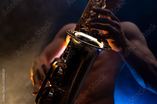 Fototapeta saksofon  muskularny-mezczyzna-z-nagim-torsem-grajacy-na-saksofonie-z-wedzonym-kolorowym-tlem