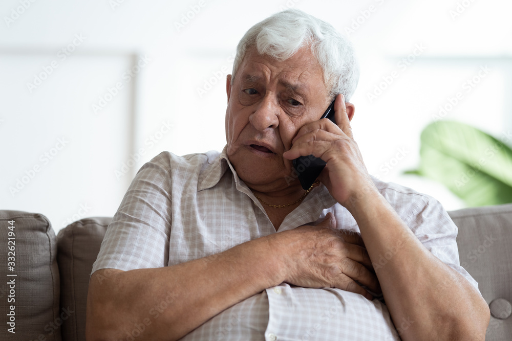 Upset older man touching chest, calling emergency, talking on phone, unhappy mature male having heart attack, lonely grandfather suffering from heartache disease at home, feeling pain, sitting alone - obrazy, fototapety, plakaty 