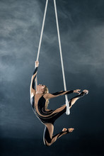 A Young Girl Performs The Acrobatic Elements In The Air Trapeze. Studio Shooting Performances On A Black Background