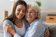 Happy mature mom and grown-up daughter sit on couch at home hug cuddle show love and care, smiling elderly mother and adult girl child embrace in living room enjoy weekend together