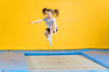 Happy little girl jumping on trampoline in fitness center