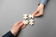 Two hands connect puzzles on a grey background. Cooperation and teamwork in business. Collaboration people for success.