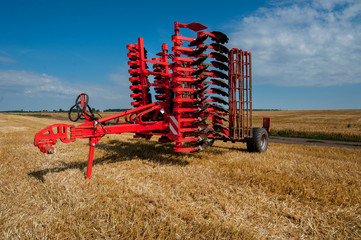 Fototapete - Red harrow folded for transportation for cultivating the land. Harrow on the field and beautiful sky background