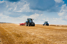 Two Blue Tractors Pulls Harrows Preoparate Arable Land, Field And Beautiful Clouds