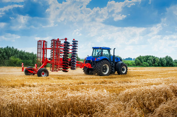 blue tractor pulls red harrow folded for transportation, arable land preparation for sowing campaign