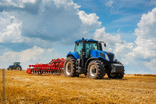 Fotografía blue new tractor with red harrow in the field against a cloudy sky, agricultural