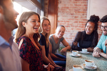 Group Of Male And Female Friends Meeting For Coffee Sitting At Table Together