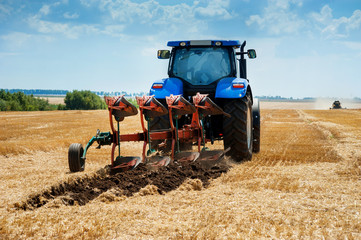 A plow attached to a blue tractor, arable land, field preparation