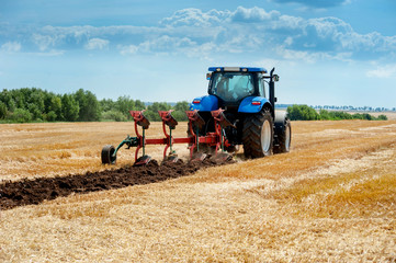 Fototapete - blue tractor pulls plow, arable land, field preparation