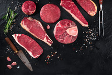 Various Cuts Of Meat, Shot From The Top On A Black Background With Salt, Pepper, Rosemary And Knives, With Copy Space