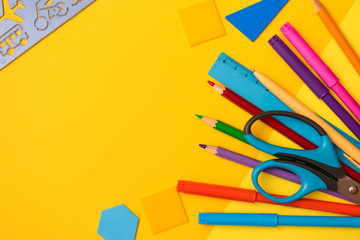 Back to school concept flat lay.Color pencils,felt pens,rulers,scissors and plastic geometric shapes on the yellow background.Copy space for text,top view