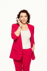 Wall Mural - Corporate Communication. Happy, cheerful businesswoman Talking On Mobile Phone in red suit and looking at camera isolated over white background.