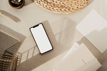Wall Mural - Flatlay of blank screen smart phone, notebooks, clips in wooden bowl, straw stand on beige concrete background. Home office desk workspace. Business, work template. Flat lay, top view.
