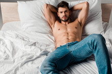 Sexy Shirtless Macho In Jeans Lying On Bed On Grey