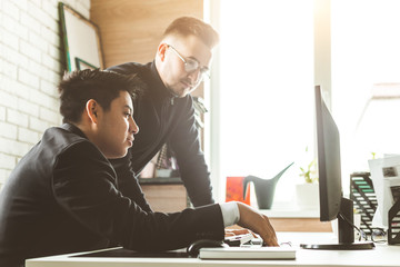 Poster - Young office worker sitting at desk, using computer. Two business man talking