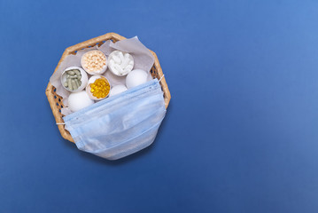 EEggs in the wicker basket on the blue background. Madical mask on the basket. Copy space. Place for text and design. Top view. Flat layout. THe eggs with pills and vitamins.              