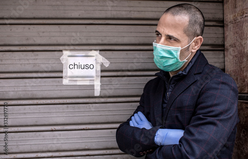 Fotografía Un uomo rasato con mascherina giacca e guanti è sconschiude la serranda della sua attività a causa delle restrizioni per la pandemia