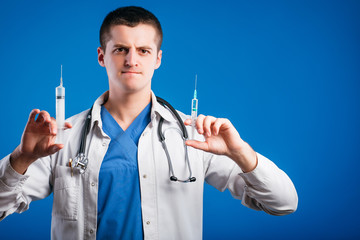 Portrait of funny emotional male doctor with two syringes isolated on blue background