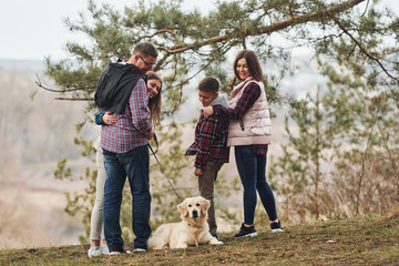 Wall Mural - Rear view of family that standing together with their dog outdoors in forest