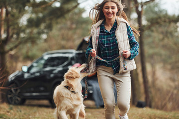 Wall Mural - Cheerful girl have walk with her dog outdoors in forest at autumn or spring season