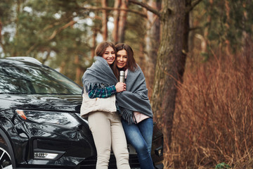 Wall Mural - Mother and daughter standing together near modern black car outdoors in the forest