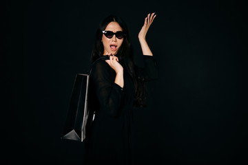 Wall Mural - Beautiful girl in sunglasses and black dress with a shopping bag on her back shows no problem. Can buy everything. Isolated on black