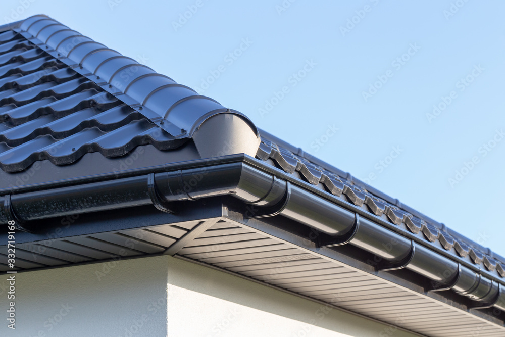 Corner of the new modern house with gutter, roof, wall under blue sky - obrazy, fototapety, plakaty 