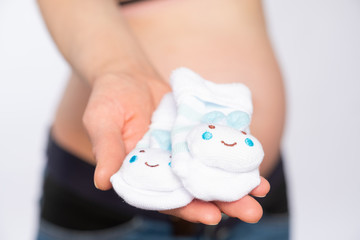 Wall Mural - Pregnant woman holds small socks on the background of the abdomen