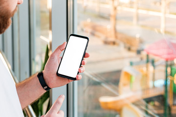 Mockup smartphone in man hand black mobile phone with blank white screen, copy space screen for your text or design or app behind the window in office with city landscape view