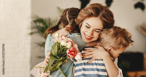 Fotografía Little children congratulating and hug mother in kitchen.