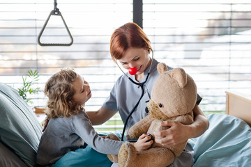 Wall Mural - Friendly female doctor examining small girl in bed in hospital.