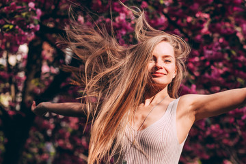 Wall Mural - Closeup portrait of a lovely girl in a park with blooming Japanese sakura trees. Romantic young blonde in a dress posing on a background of spring flowering trees. Cherry blossoms.