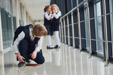 Boy sitting on the floor. School kids in uniform together in corridor