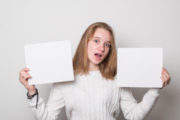 Wall Mural - Positive girl holds a blank poster for text. Schoolgirl with a smile holds a white sheet for text.