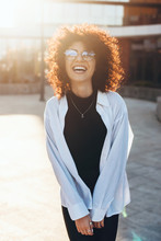 Charming Caucasian Woman With Curly Black Hair Smiling And Cheering Outside While Wearing Eyeglasses And White Shirt