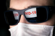 © scaliger - COVID-19 coronavirus concept, computer screen with COVID19 warning reflects in man glasses. Person in face mask looks news about corona virus outbreak.
