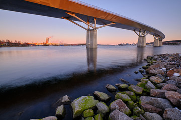 Wall Mural - Big bridge going over a cove with stones foreground and a city in the background