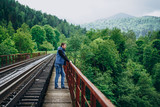 Fototapeta Miasto - Young man on railway track on forest background. The observation deck.