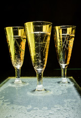 Glasses of champagne  luminous golden light black table wet  with black background.