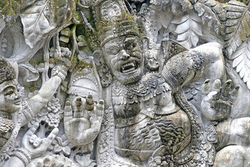 Stone wall with Balinese demons and gods, heros of Hindu mythology.